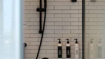 A modern shower with a rain showerhead, handheld showerhead, and a handheld massager. There are three bottles of shampoo and conditioner on the wall.