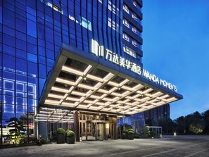 A modern hotel entrance with a glass facade, a covered entrance area, and a sign reading "Wanda Moments". - Wanda Moments NingBo (Ningbo)