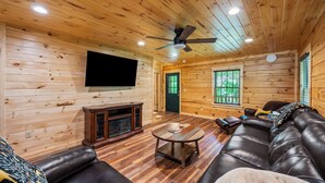 A log cabin interior with a leather sofa, a coffee table, a fireplace, and a ceiling fan. - Main Channel Lots of Water. Escape to The Getaway at Pine Haven — a spotless log cabin on Smith Mountain Lake where every bedroom has its own en-suite bath. Enjoy lake views, a stocked kitchen, fire pit, pool table, and dock access. (Union Hall)