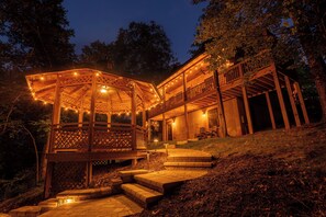 A wooden gazebo with string lights, a covered porch, and a staircase leading to a deck.
