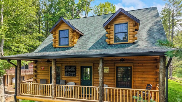 A log cabin with a porch, two windows, and a sign with rules. - Main Channel Lots of Water. Escape to The Getaway at Pine Haven — a spotless log cabin on Smith Mountain Lake where every bedroom has its own en-suite bath. Enjoy lake views, a stocked kitchen, fire pit, pool table, and dock access. (Union Hall)
