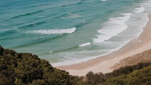 Una playa con aguas turquesas cristalinas, una orilla arenosa y abundante vegetación en primer plano.