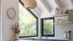 Una cocina moderna con una isla grande, taburetes de bar, una lámpara colgante y un ventanal con vistas a árboles.