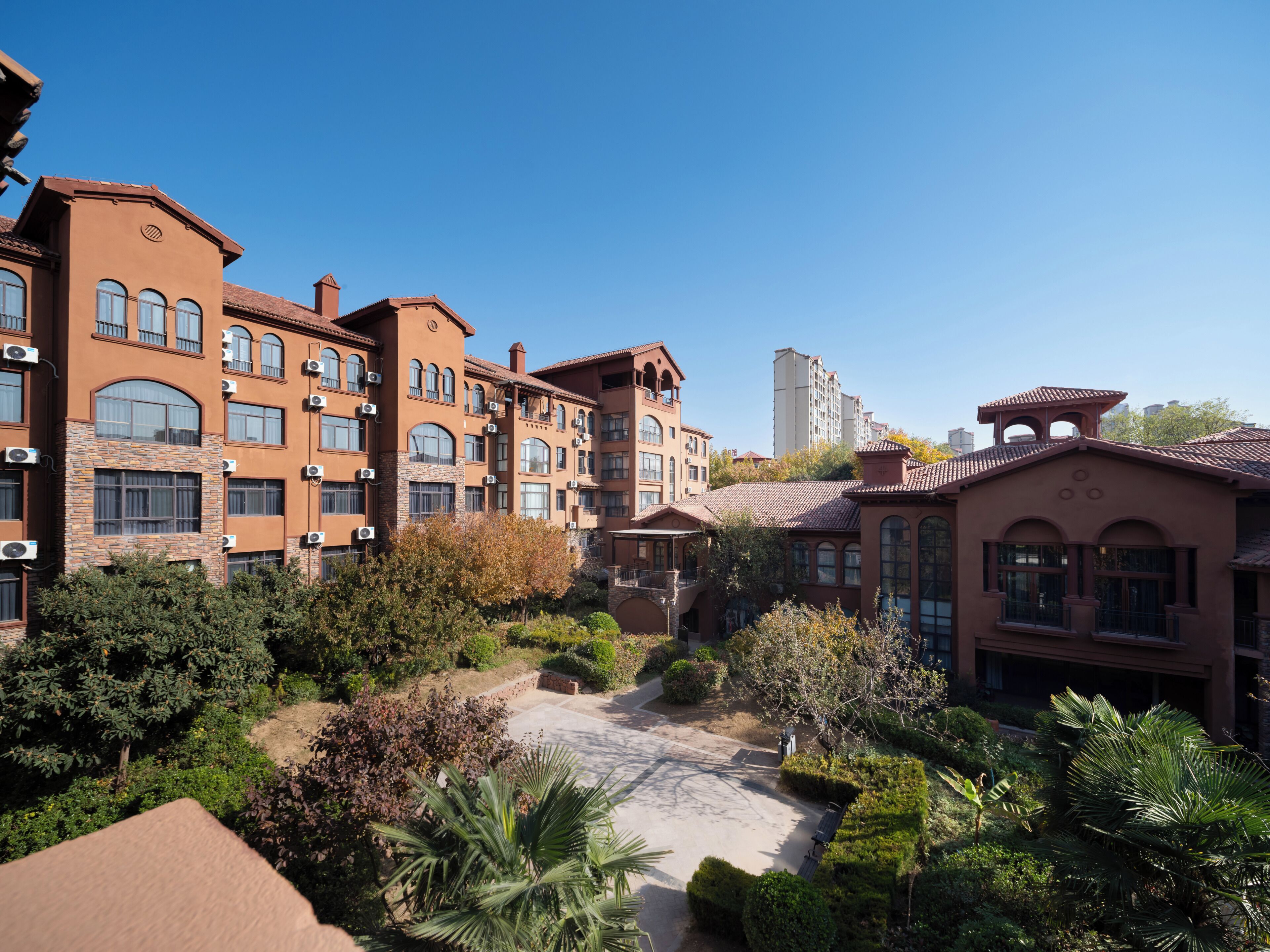 Un edificio de varios pisos con balcones, unidades de aire acondicionado y un patio con diversas plantas.
