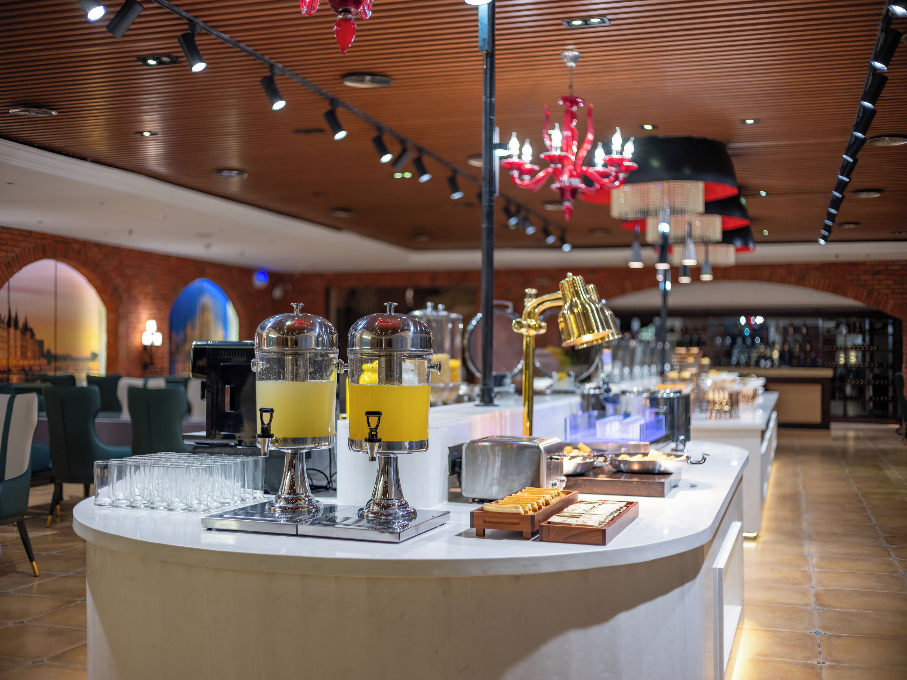 A bar area with a counter, two beverage dispensers, a golden faucet, and a red chandelier.