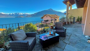 Una terrazza con mobili in vimini, un tavolo con un vaso di fiori e vista su un lago e montagne.
