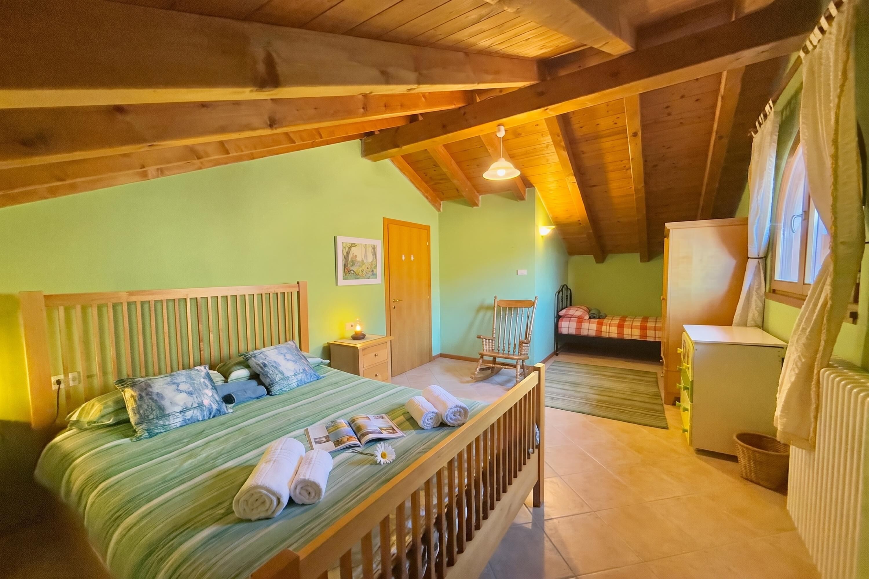 Une chambre mansardée chaleureuse, avec un lit, une chaise, un radiateur et une fenêtre avec des rideaux.