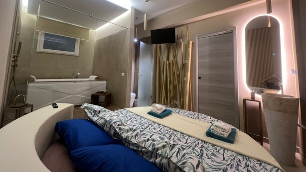 A modern hotel room with a curved bed, a large mirror, a bathtub, and a shower area. - Charming deluxe suite 2 steps from the sea and downtown (Terrasini)