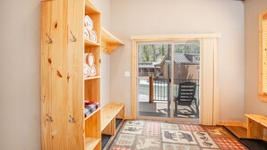 A wooden wardrobe with shelves and hooks, a bench, a patterned rug, and a sliding glass door leading to an outdoor deck. - Chalet w 2nd Floor | Pool, Hot Tub (Breckenridge)