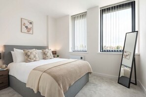 A bedroom with a bed, bedside tables, a window with blinds, a mirror, and a wall-mounted artwork.