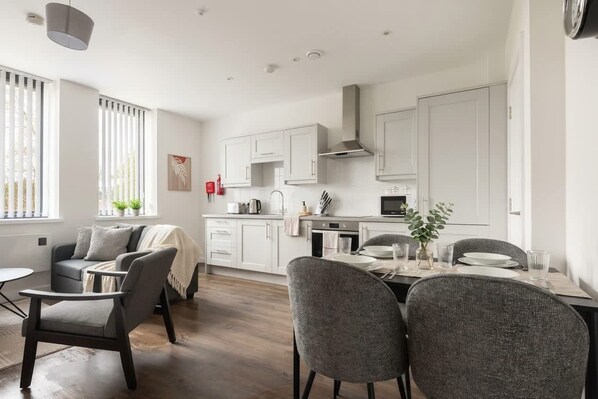 A modern kitchen with white cabinets, a dining table set for four, and a living area with a sofa and a coffee table.