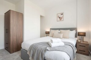 Une chambre à coucher comprenant un lit, des tables de chevet, une armoire et une œuvre d’art accrochée au mur.