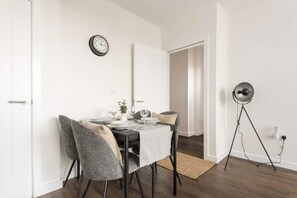 A dining area with a table set for four, a clock on the wall, and a floor lamp.