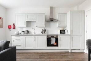 A modern kitchen with white cabinets, a stainless steel range hood, and a built-in oven.