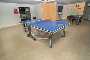 Ein Tischtennis-Tisch mit Netz, ein Billardtisch und eine Tür mit einem Schild.