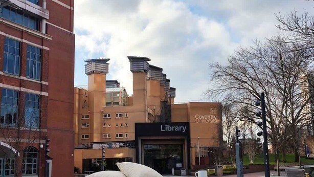 Un edificio biblioteca con un cartello evidente, circondato da architetture moderne e un'area verde.