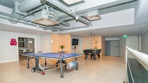 Un'ampia area interna con tavolo da ping pong, tavolo da biliardo e televisore a parete.