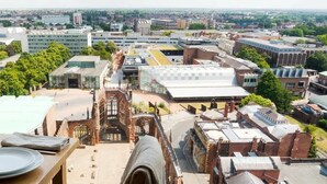 Vista dall'alto su una città con edifici moderni, un ponte storico e un'area ristorazione con un tavolo apparecchiato per due.