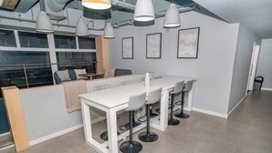 Un interno moderno con un tavolo bianco e sgabelli da bar, illuminazione a sospensione e opere d'arte incorniciate alle pareti.
