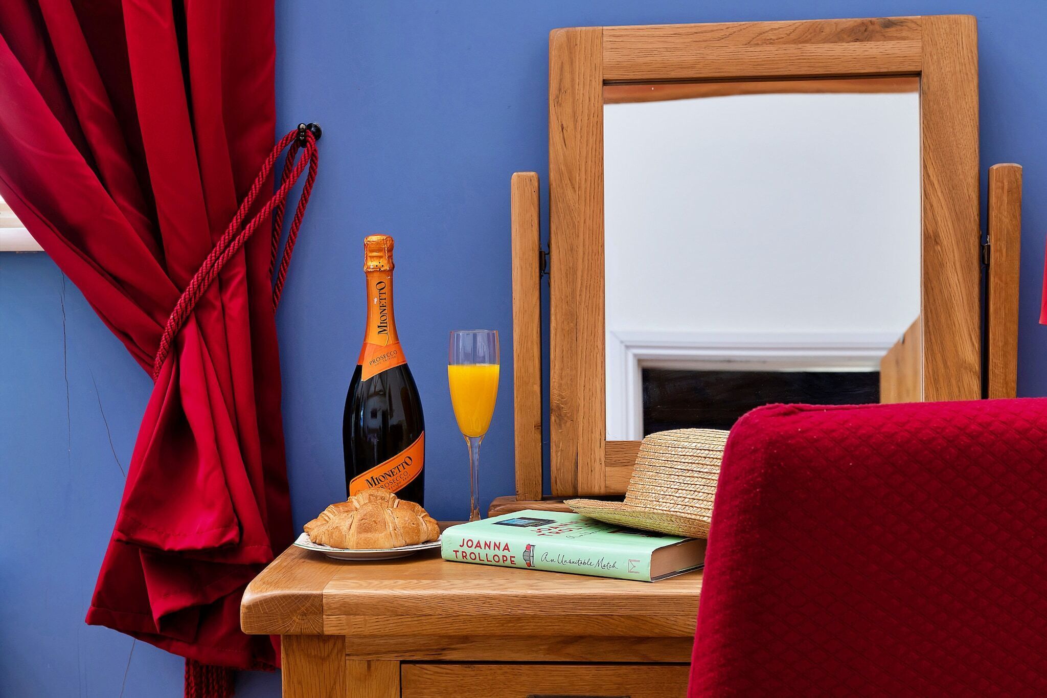 A wooden bedside table with a book, a bottle, and a glass of orange juice.
