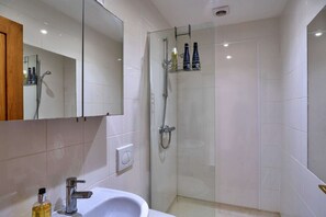 Een moderne badkamer met een douchecabine van glas, een witte wastafel en een spiegel boven de wastafel.