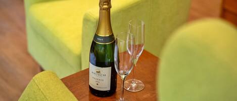 A bottle of champagne and an empty glass on a wooden table in a room with a yellow armchair.