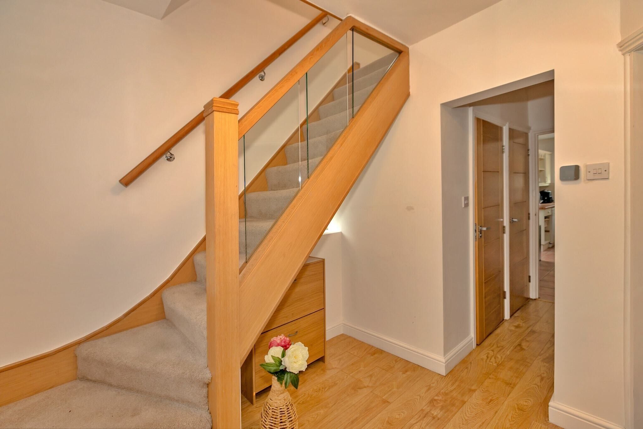 A wooden staircase with glass railings and a small wooden cabinet at the bottom.