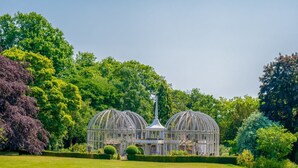 Une serre dotée d’une tour centrale, entourée de haies bien entretenues et d’une variété d’arbres.