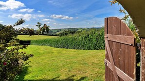 A wooden gate leading to a lush green landscape with rolling hills and a clear blue sky.