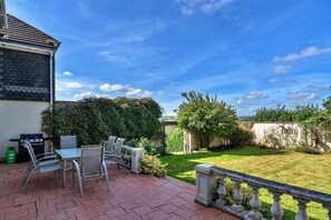 A patio with a grill, chairs, and a view of a garden. - Cottage in Whitestone with Garden & Games Room (Whitestone)