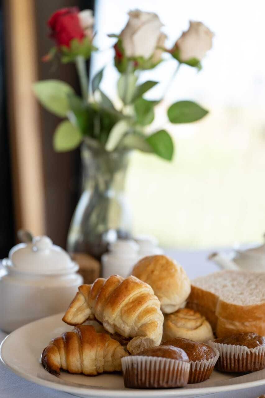 A plate with croissants and muffins, a vase with roses, and a teapot on a table.