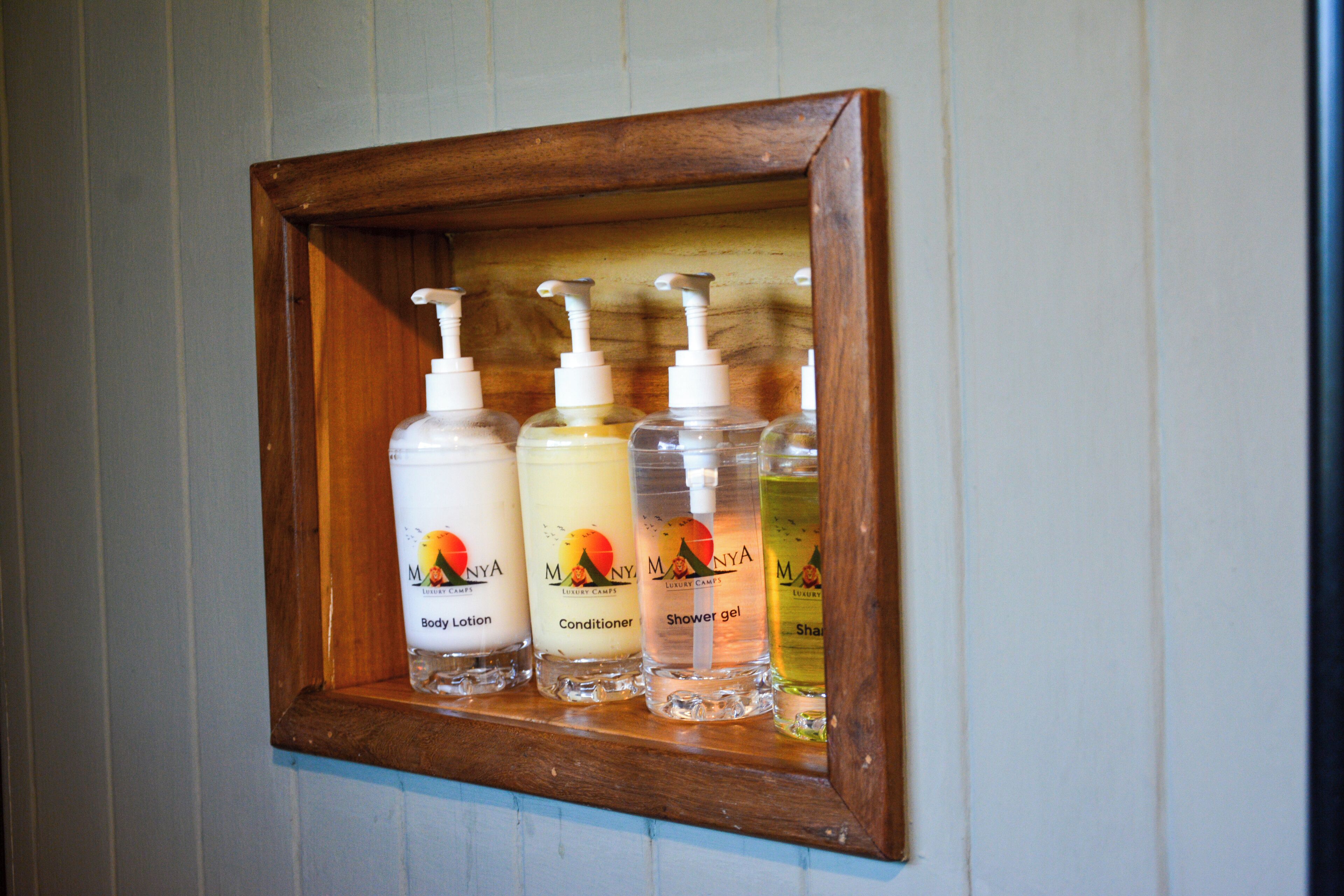 A wooden-framed shelf with three bottles of Monya body lotion, conditioner, and shower gel.
