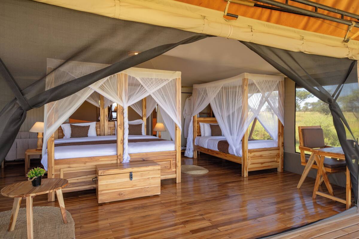A wooden tent with two beds, each with a canopy, a small table, and a chair.