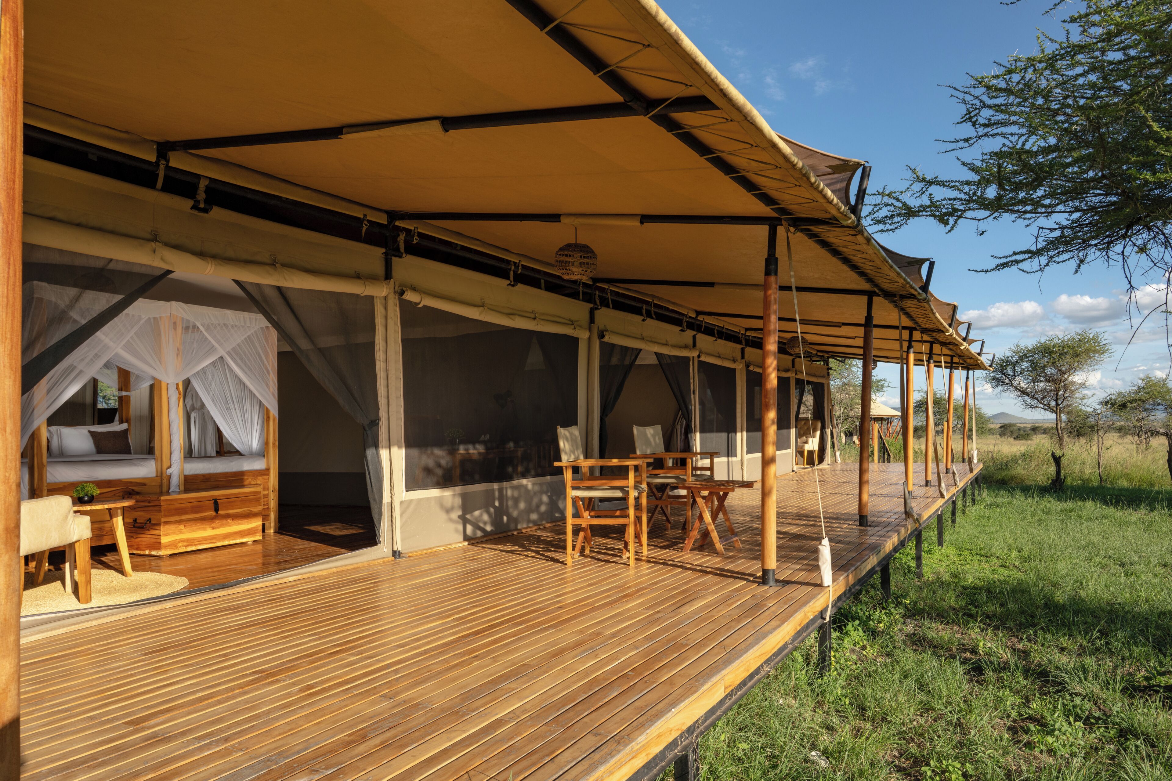 Une terrasse en bois dotée d’un espace salon couvert, un lit pourvu d’une moustiquaire et une vue sur le paysage environnant.