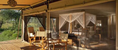 A tented accommodation with a wooden deck, outdoor seating, and a view of the surrounding greenery.