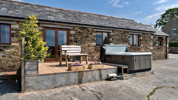 A stone building with a patio area, including a hot tub, wooden furniture, and potted plants. - Countryside cottage with private hot tub, No Deposit (Liskeard)