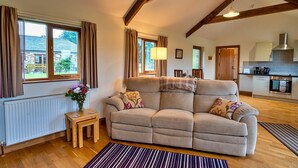 A cozy living room with a sofa, a small table with a vase of flowers, and a view of the kitchen and outside. - Countryside cottage with private hot tub, No Deposit (Liskeard)