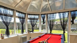 Une table de billard dans une véranda, avec vue sur un jardin et une statue.