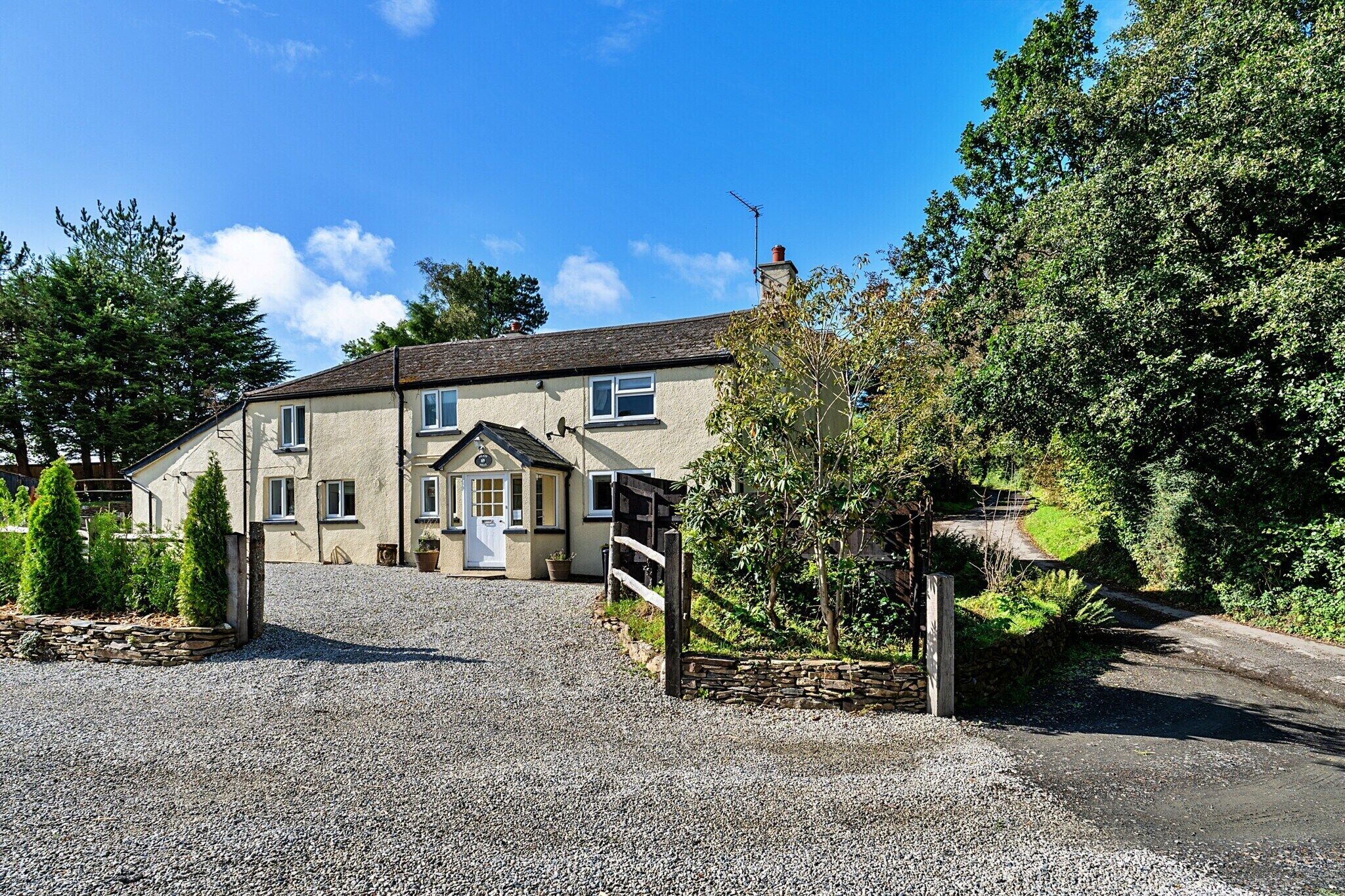 A two-story house with a gravel driveway leading to a wooden gate.