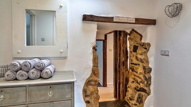 Een badkamer met een spiegel, een handdoekhouder, een stenen muur en een houten balk met een bordje.