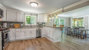 A spacious kitchen with white cabinetry, a central island, and a dining area with wooden chairs. - Beautiful White Mountains Home w/ Sauna, Firepit and  Gameroom Local Skiing, Hiking and Golf. (Thornton)