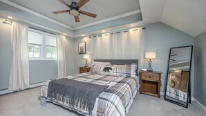 A bedroom with a large bed, a ceiling fan, two bedside tables with lamps, a mirror, and a window with curtains. - Beautiful White Mountains Home w/ Sauna, Firepit and  Gameroom Local Skiing, Hiking and Golf. (Thornton)