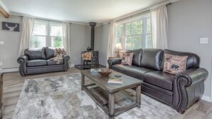 A living room with two leather sofas, a coffee table, a fireplace, and a large window with curtains. - Beautiful White Mountains Home w/ Sauna, Firepit and  Gameroom Local Skiing, Hiking and Golf. (Thornton)