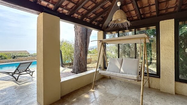 Ein überdachter Außenbereich mit Schaukelstuhl, Pool und Landschaftsblick.