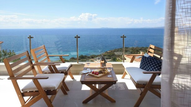 A terrace with wooden chairs and a table, overlooking the sea.