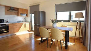 A modern kitchen with wooden cabinets, a stainless steel refrigerator, and a dining area with two chairs and a table.