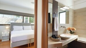 A modern bedroom with a bed, bedside table, and a large mirror above a bathroom vanity.
