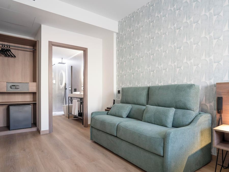 A modern living room with a green sofa, a wooden cabinet with a safe, and a bathroom visible through an open door.