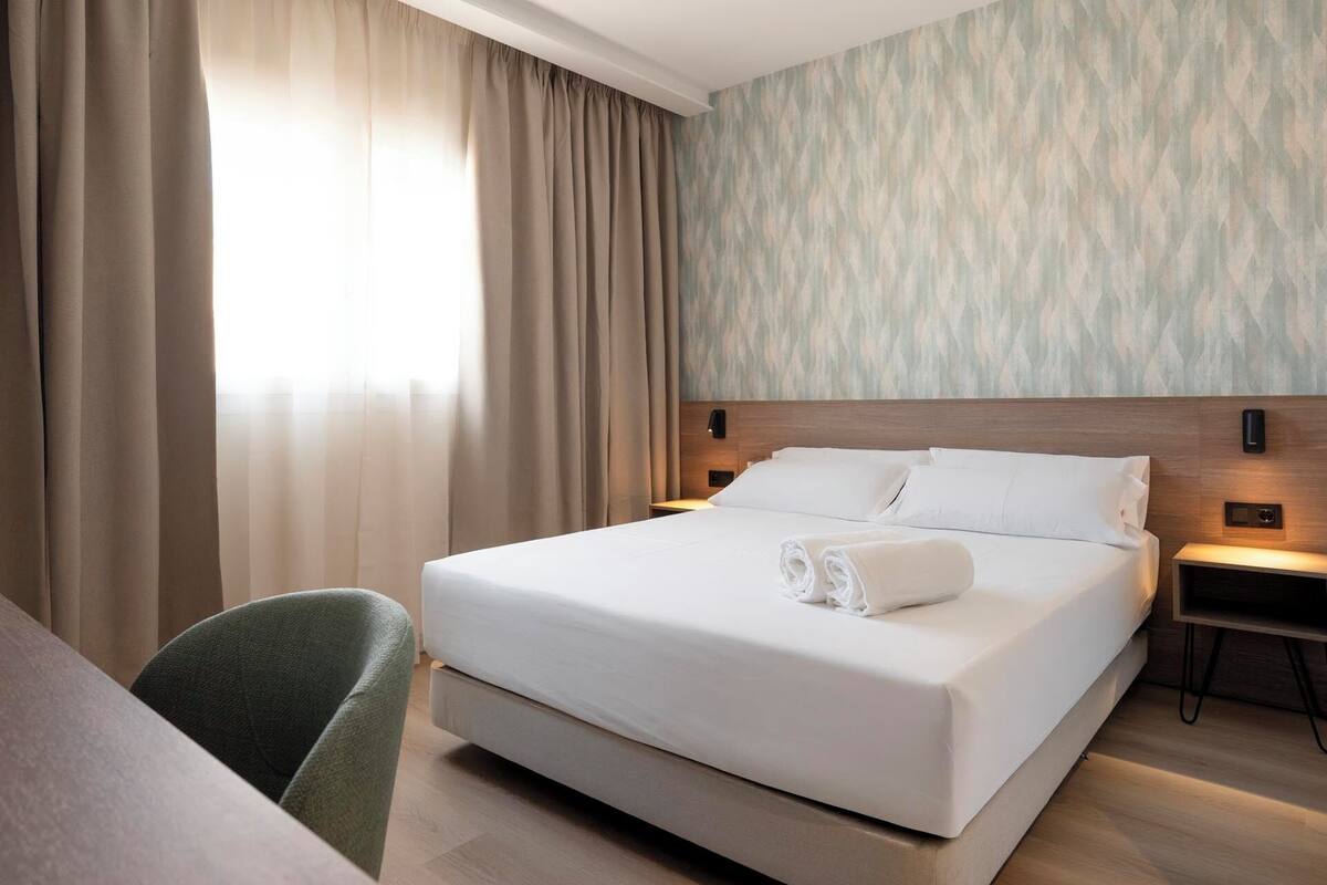 A hotel room with a large bed, a desk, and a chair. There are two bedside tables with lamps.