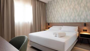 Een hotelkamer met een groot bed, een bureau en een stoel. Er zijn twee nachtkastjes met lampen.